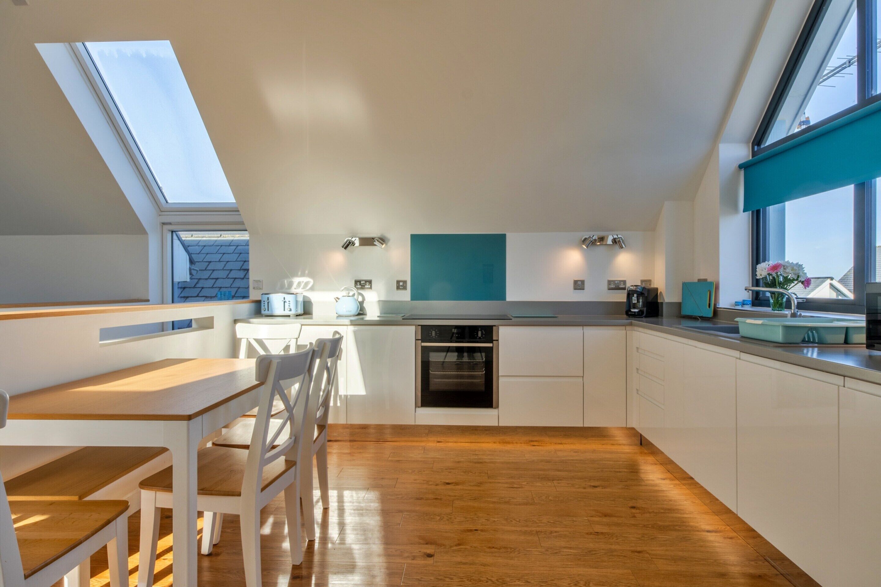A modern kitchen with a skylight, wooden flooring, and white cabinetry.