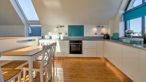 A modern kitchen with a skylight, wooden flooring, and white cabinetry. - Westward Ho Seaside Stay ( (Bideford)