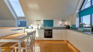 A modern kitchen with a skylight, wooden flooring, and white cabinetry.