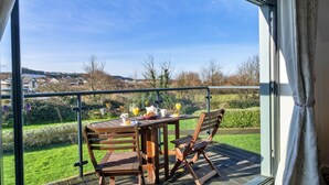 A balcony with a table set for breakfast, including croissants and orange juice, overlooking a green landscape. - Westward Ho Seaside Stay ( (Bideford)
