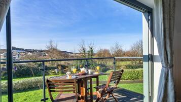 A balcony with a table set for breakfast, including croissants and orange juice, overlooking a green landscape.