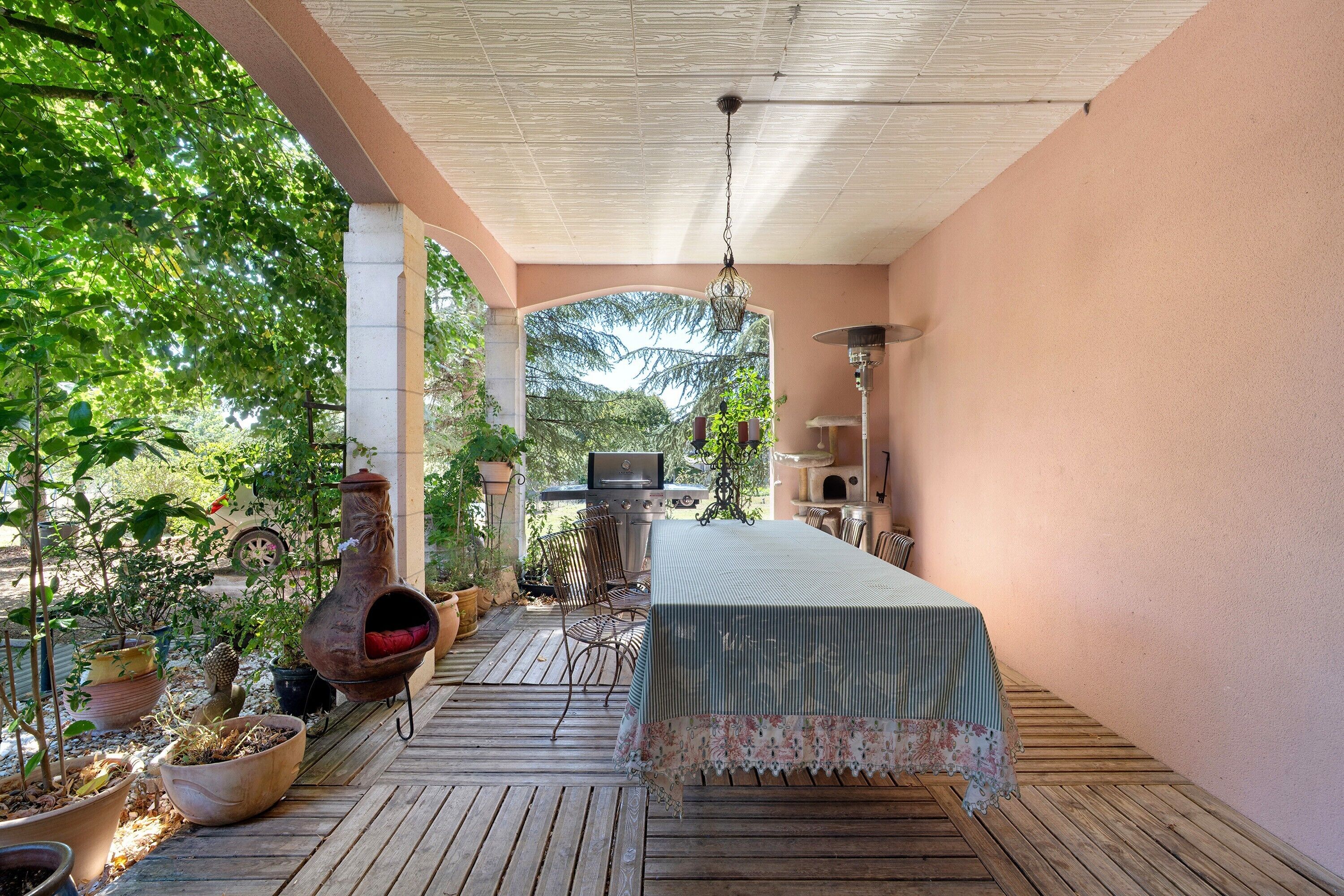 An outdoor patio with a table, chairs, a grill, and potted plants.