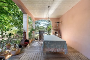 Een terras buiten met een tafel, stoelen, een barbecue en potplanten.