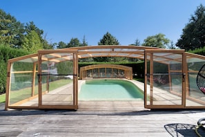 Een zwembad met glazen omheining, een houten terras en een pergola van hout.