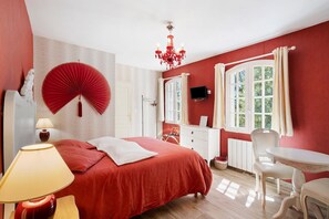 Un dormitorio con cama, escritorio, silla, candelabro y ventana con cortinas.