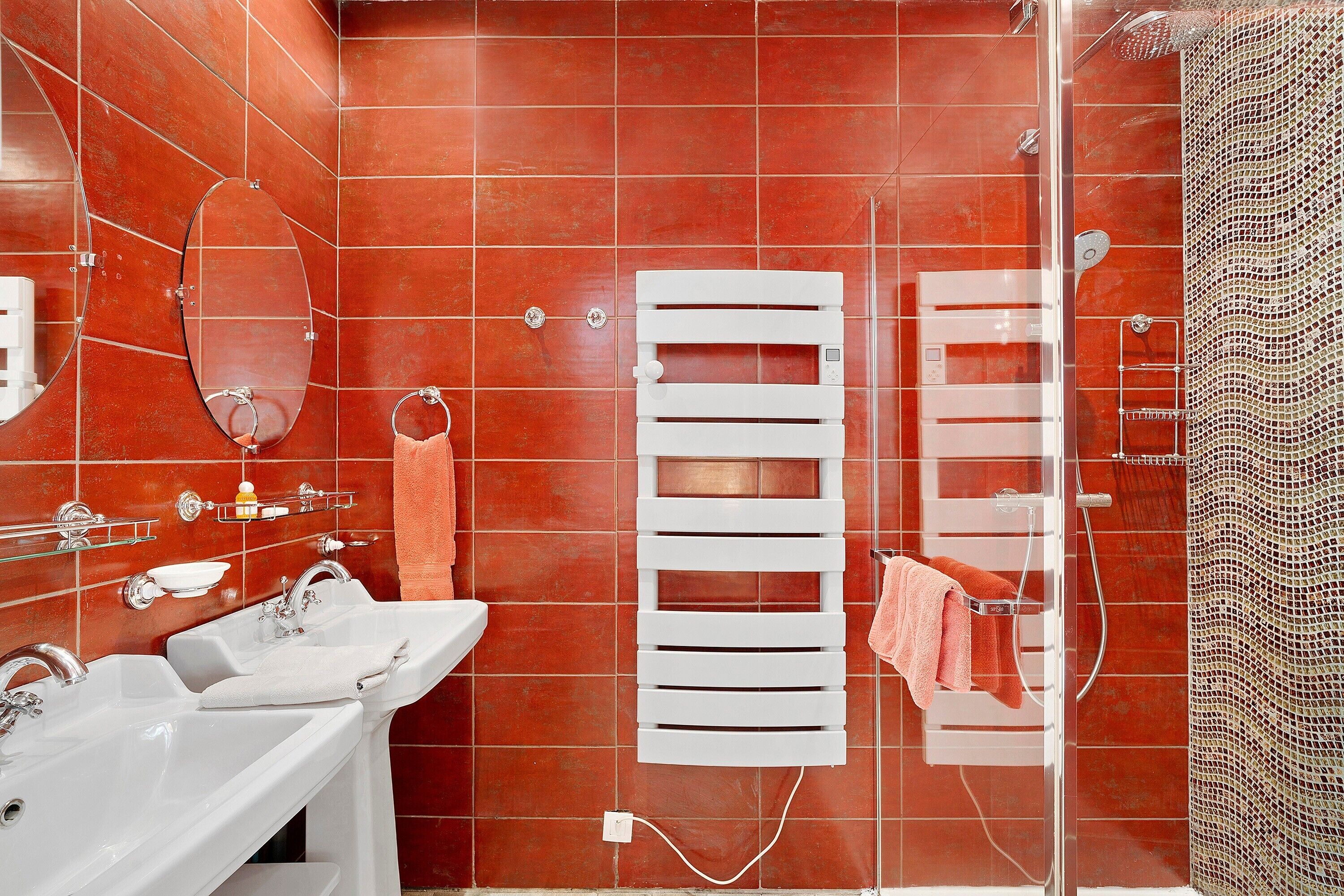 A bathroom with a white bathtub, a sink, a glass shower enclosure, and a towel rack with towels.