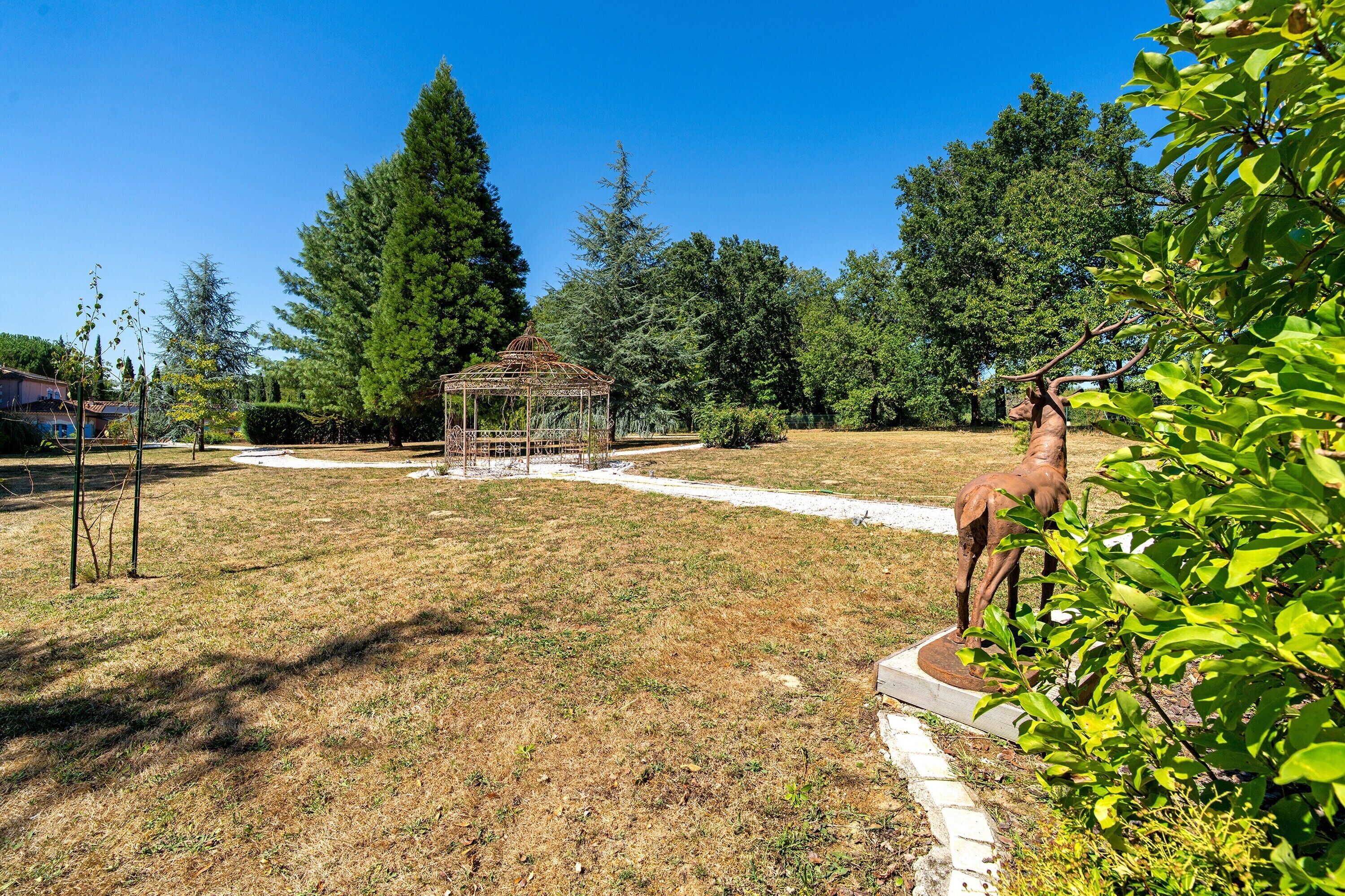 A garden with a gazebo, a statue, and a variety of trees.