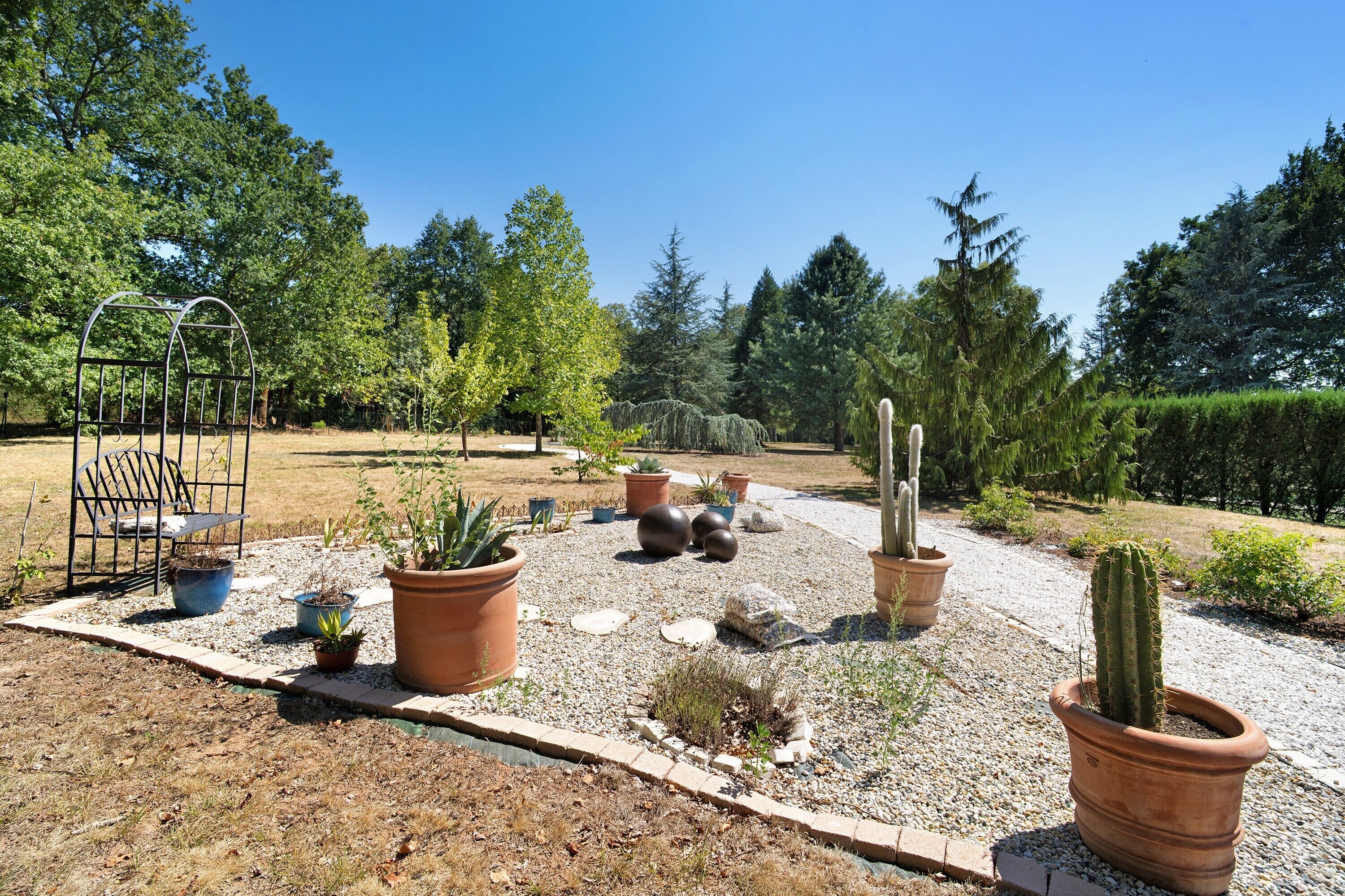 Un jardin agrémenté de diverses plantes en pot, d’un banc en métal et d’un chemin recouvert de gravier.