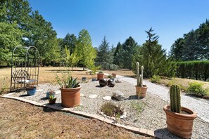 Un jardín con plantas en macetas, un banco de metal y un camino de grava.