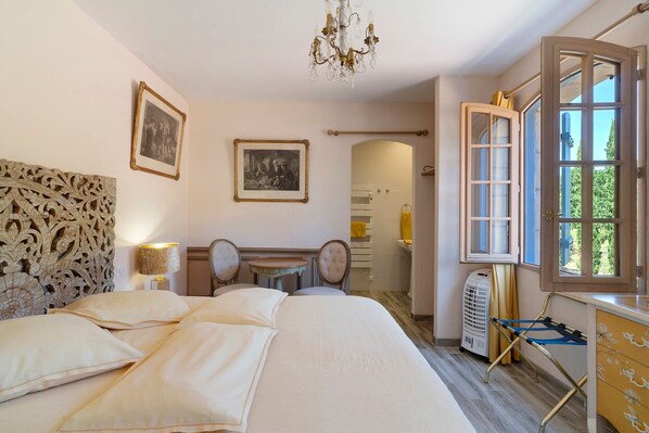 Un dormitorio con una cama grande, dos sillones, una mesa, una araña y una ventana con vistas.