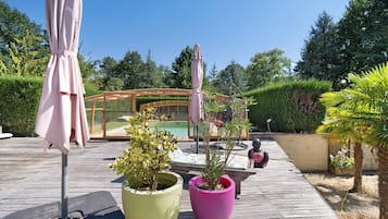 Un terrazzo in legno con piante in vaso, mobili da esterno e un'area vetrata con piscina.
