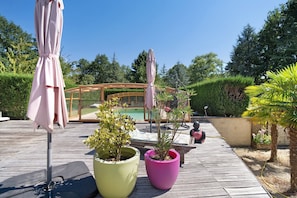 A wooden deck with potted plants, outdoor furniture, and a glass-enclosed area with a pool. - La table de pierre – Adalgisa Room – Table d'Hôte (Lussas-et-Nontronneau)