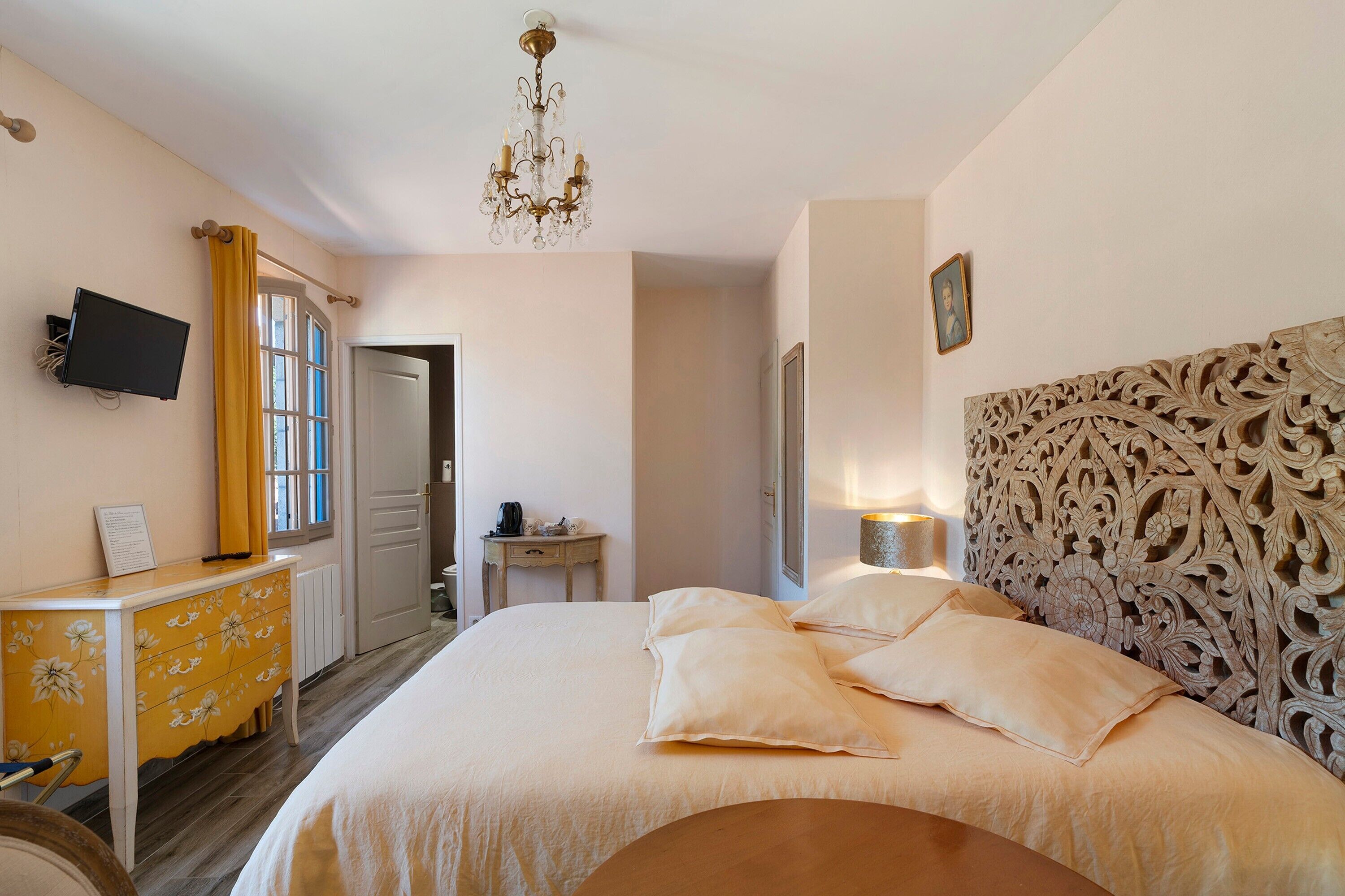 Una camera d'albergo con un letto, una scrivania, una sedia, una televisione e un lampadario.