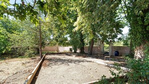 Un área de grava rodeada de árboles, con un banco y un muro al fondo.
