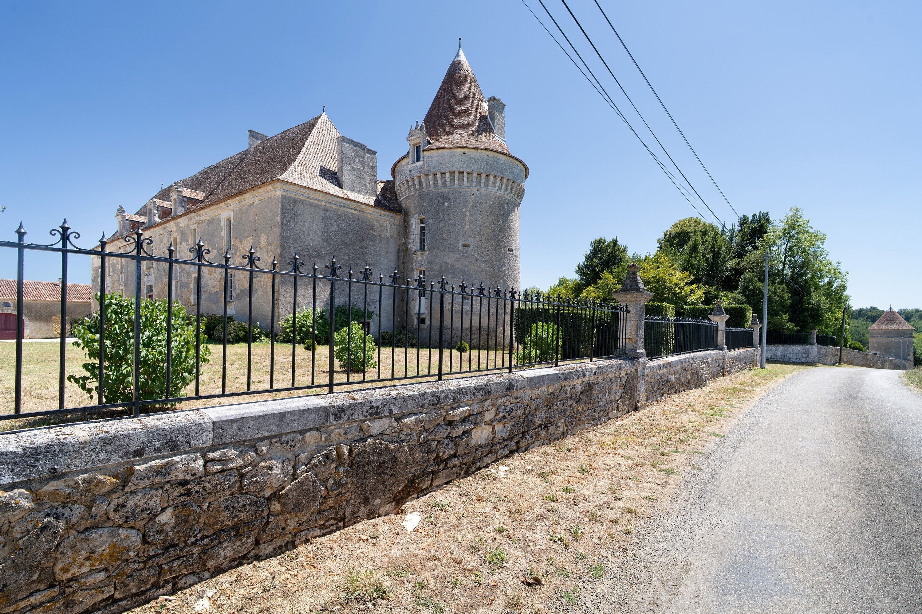 Un edificio de piedra histórico con una torre destacada, rodeado por un muro de piedra y una cerca de metal.