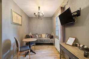 Ein gemütliches Zimmer mit einem Bett, einem Tisch, Stühlen, einer Chandelierleuchte, einem Fernseher und einem gerahmten Zertifikat an der Wand.