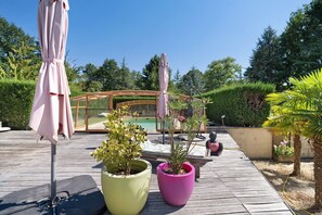 A wooden deck with potted plants, outdoor furniture, and a glass-enclosed area with a pool.