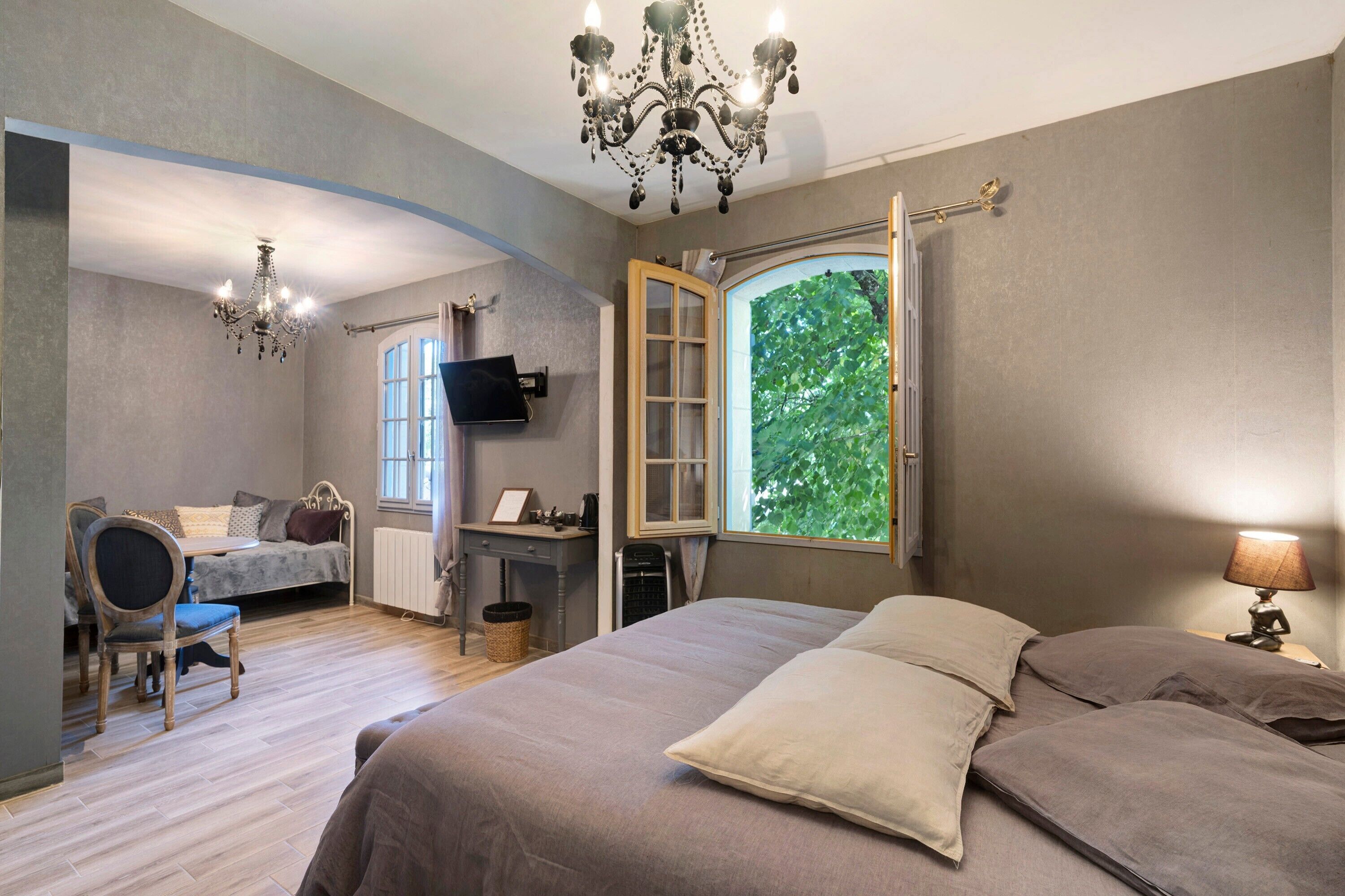 Une chambre à coucher avec un grand lit, un bureau, une chaise, une télévision et une fenêtre donnant sur les arbres.