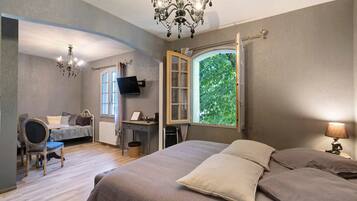 Une chambre à coucher avec un grand lit, un bureau, une chaise, une télévision et une fenêtre donnant sur les arbres.