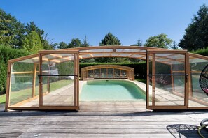 A glass-enclosed swimming pool with a wooden deck and a wooden pergola structure. - La table de pierre – Dalila Room (Lussas-et-Nontronneau)