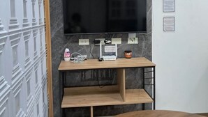 A modern living room with a flat-screen TV mounted on a marble wall, a wooden TV stand with electronic devices, a round wooden table, and a decorative plate on the wall. - City View Studio - Pool · Gym - Caesar Residence (Lapu-Lapu)