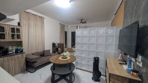 A compact living space with a kitchenette, a sofa, a dining area, and a TV mounted on the wall. - City View Studio - Pool · Gym - Caesar Residence (Lapu-Lapu)