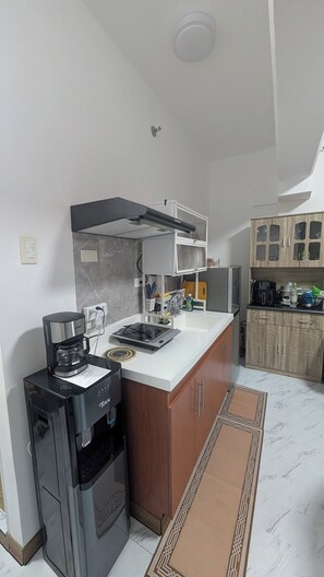 A compact kitchen with a built-in stove, coffee maker, and wooden cabinets. - City View Studio - Pool · Gym - Caesar Residence (Lapu-Lapu)