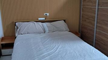 Een moderne slaapkamer met een houten hoofdbord, een bed met een beddengoed met een patroon, een nachtkastje en een stopcontact.