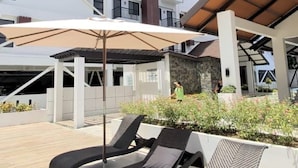 A rooftop lounge area with sun loungers and umbrellas, surrounded by a high-rise building with balconies. - City View Studio - Pool · Gym - Caesar Residence (Lapu-Lapu)