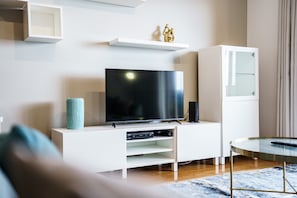 Ein modernes Wohnzimmer mit einem Flachbildfernseher auf einer weißen Unterhaltungsanlage, einem Glastisch und einem kleinen runden Tisch mit einer Fernbedienung.