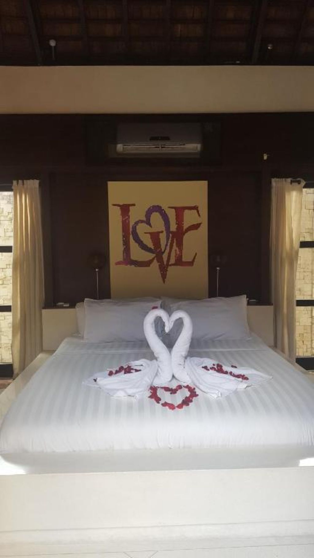 A bed with a heart-shaped towel arrangement and a 'LOVE' sign on the wall.