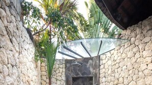 Área externa com paredes de pedra e porta de vidro que dá para um chuveiro.