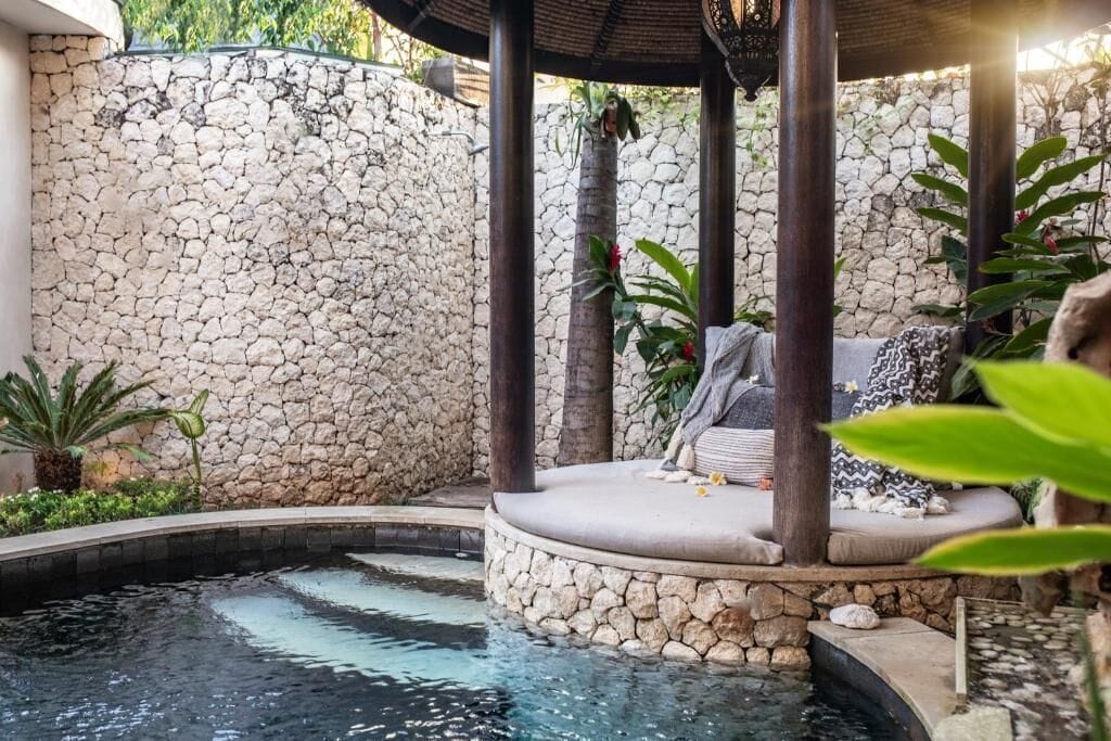 A stone wall, a circular seating area with cushions, and a small pool.
