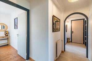 A hallway with a wooden floor, a radiator, a framed picture, and a door with a black frame. - Le Roz Cocoon - Hypercentre à 10mn de la plage (Perros-Guirec)