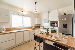 A modern kitchen with white cabinetry, a wooden countertop, a built-in dishwasher, a microwave, a stove, and a refrigerator. - Le Roz Cocoon - Hypercentre à 10mn de la plage (Perros-Guirec)
