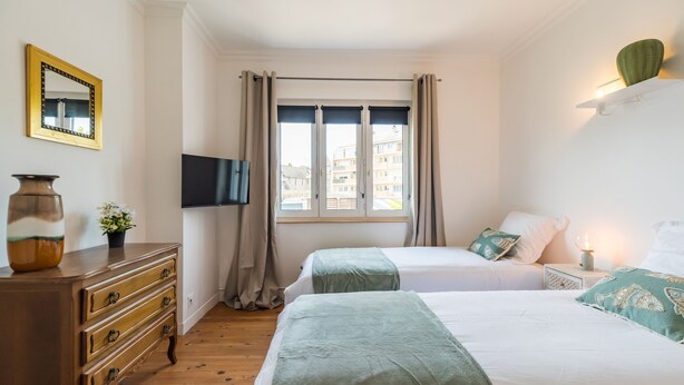 Ein Hotelzimmer mit zwei Betten, einem Schminktisch, einem Flachbildfernseher und einem Fenster mit Vorhängen.