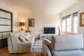 A modern living room with a sofa, a television, and a window with blinds. - Le Roz Cocoon - Hypercentre à 10mn de la plage (Perros-Guirec)