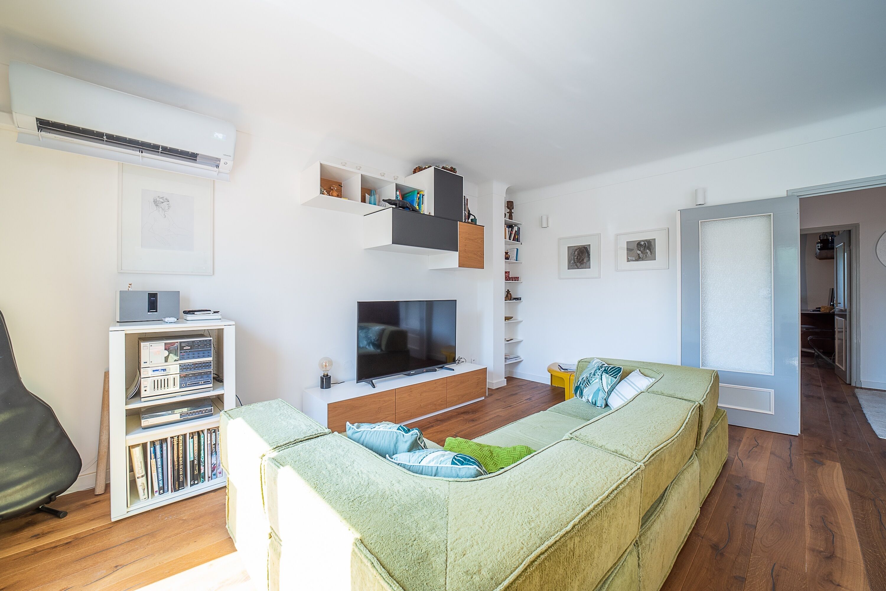 A modern living room with a flat-screen TV, a sofa, a bookshelf, and a dining area.