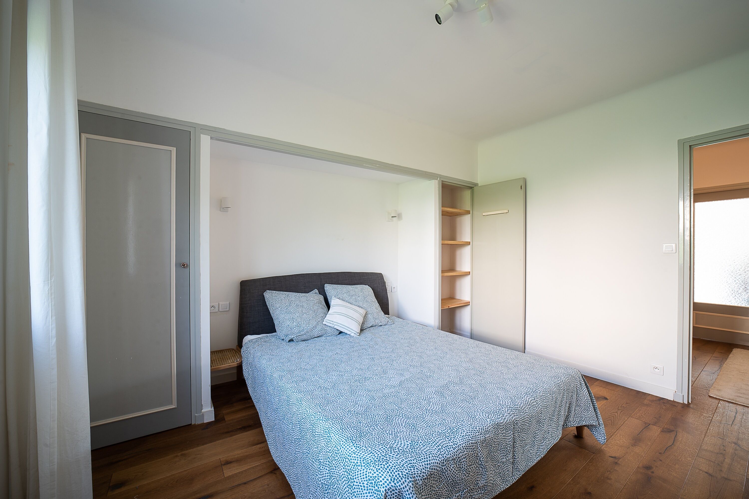 A bedroom with a bed, a wardrobe, a built-in shelf unit, and a window.