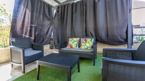 An outdoor seating area with a covered patio, a sofa with colorful cushions, and two chairs.