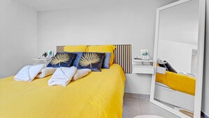 A bedroom with a bed, pillows, a bedside table, a wardrobe, and a mirror.