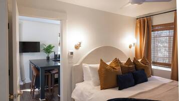 Una habitación de hotel con cama, escritorio, televisor y ventilador de techo.