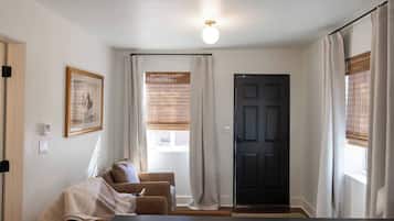A room with a dark door, a window with blinds, a framed picture on the wall, and a sofa with a blanket.
