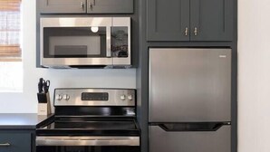 Cocina con horno de acero inoxidable, microondas y refrigerador, y armarios oscuros.