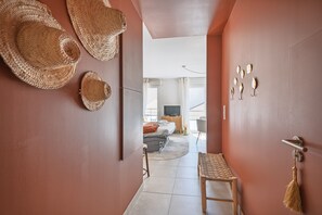 A hallway with woven baskets on the wall, a wooden bench, and a view into a room with a bed and a television. - L'Écrin Baco - À 700 m de la gare (Nantes)