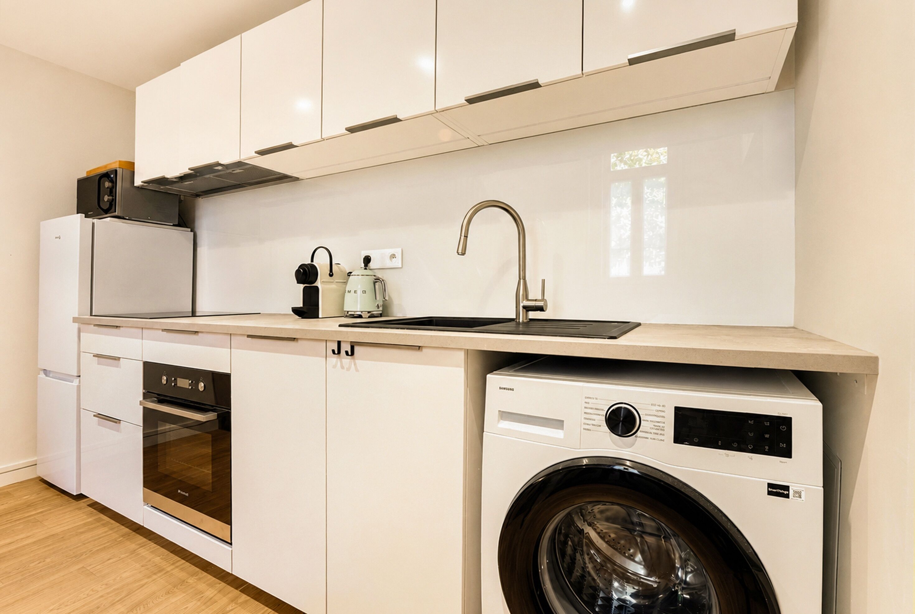 Una cocina compacta con lavadora integrada, microondas y fregadero.