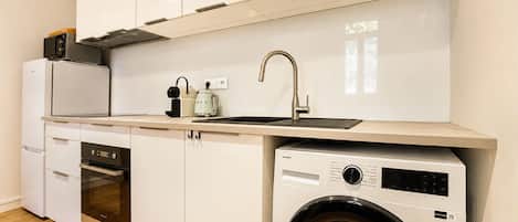 Una cocina compacta con lavadora integrada, microondas y fregadero.