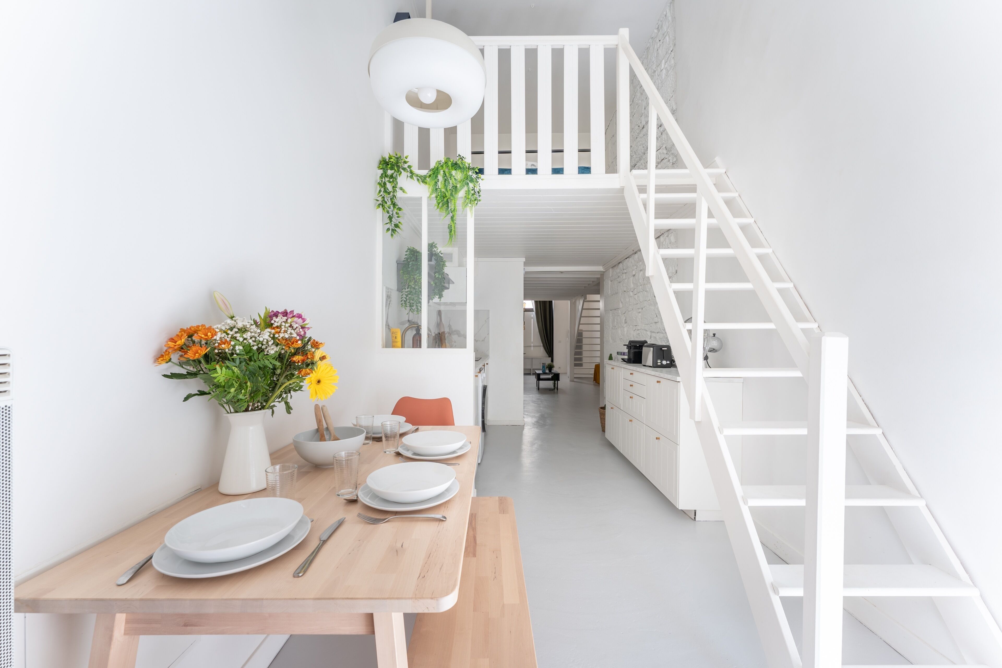 A modern kitchen with white cabinetry, a wooden dining table set for four, and a staircase leading to an upper level.