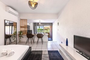 A modern hotel room with a bed, a TV, a desk, and a view of the garden. - La Plage d'Irène (Appartement n°36) - Avec balcon (San-Nicolao)