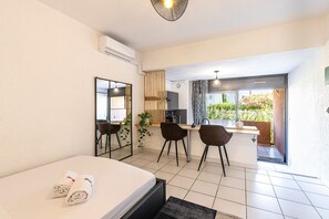 A hotel room with a bed, a desk, two chairs, a mirror, and a view of the outside. - La Plage d'Irène (Appartement n°36) - Avec balcon (San-Nicolao)